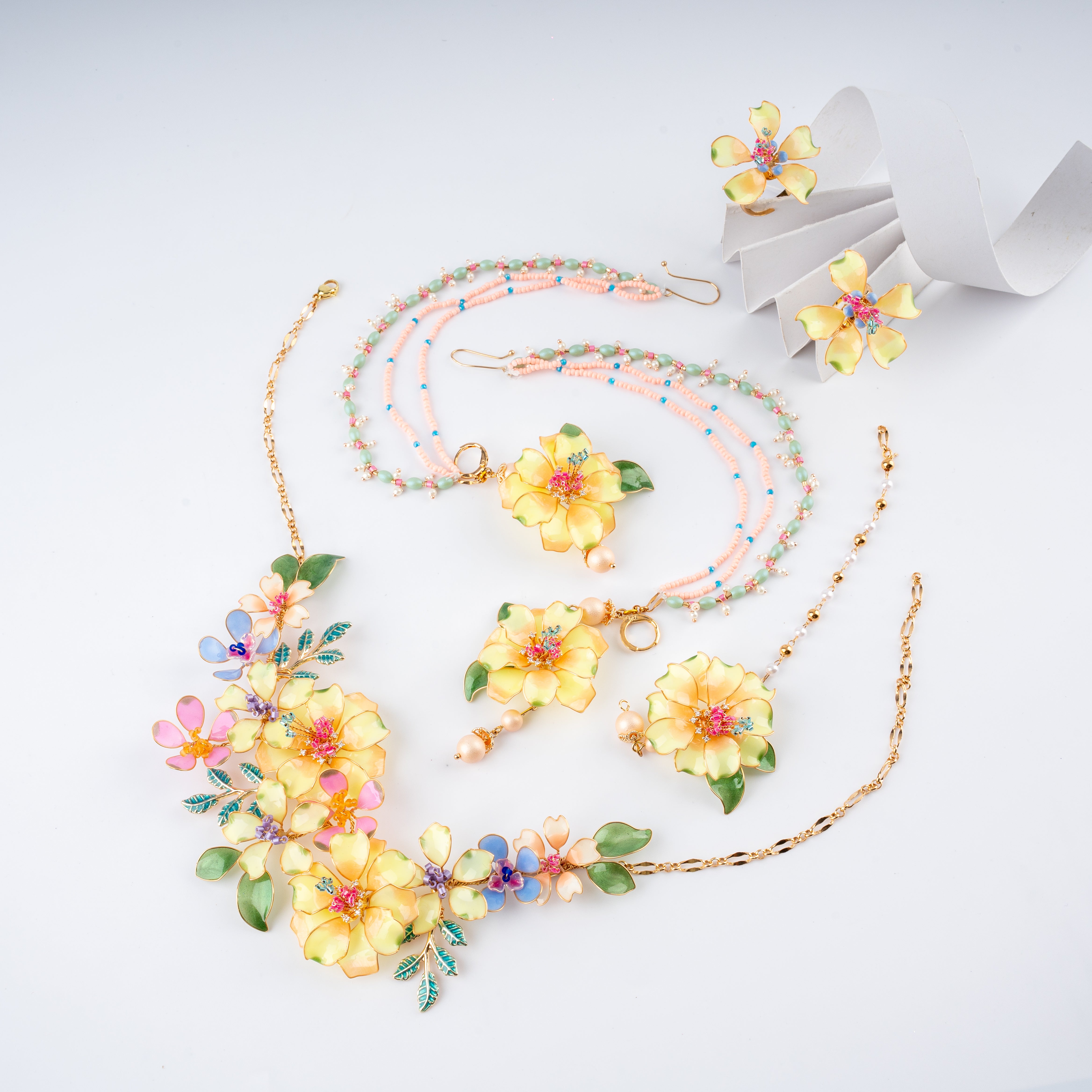 Yellow and pastel floral resin art jewelry set with necklace, multi-strand beaded chain earrings, maang tikka, and rings from US Catalog.   