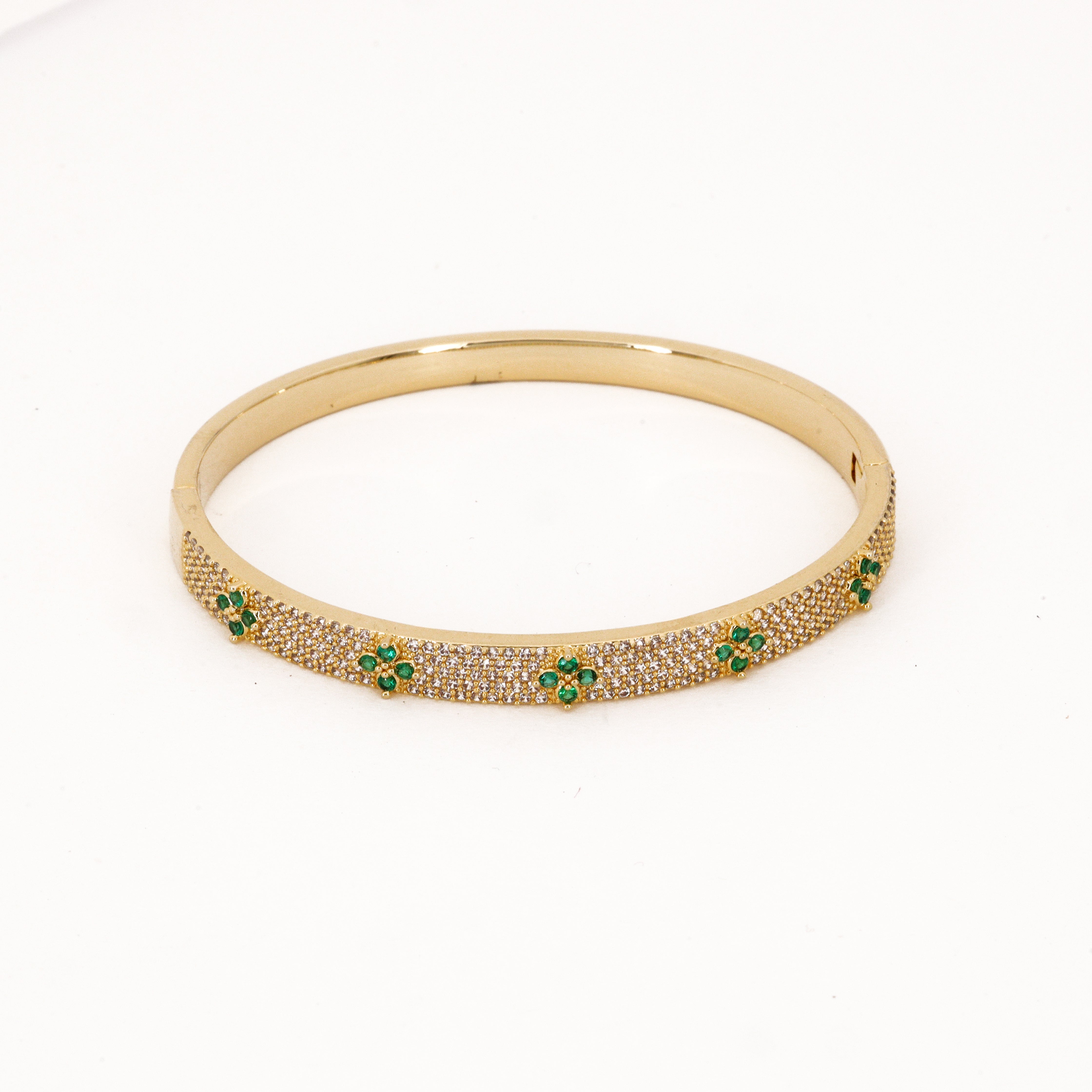 Gold tone rigid bangle bracelet encrusted with cleaR crystals and green emerald floral accents on a plain white background for US Catalog.
