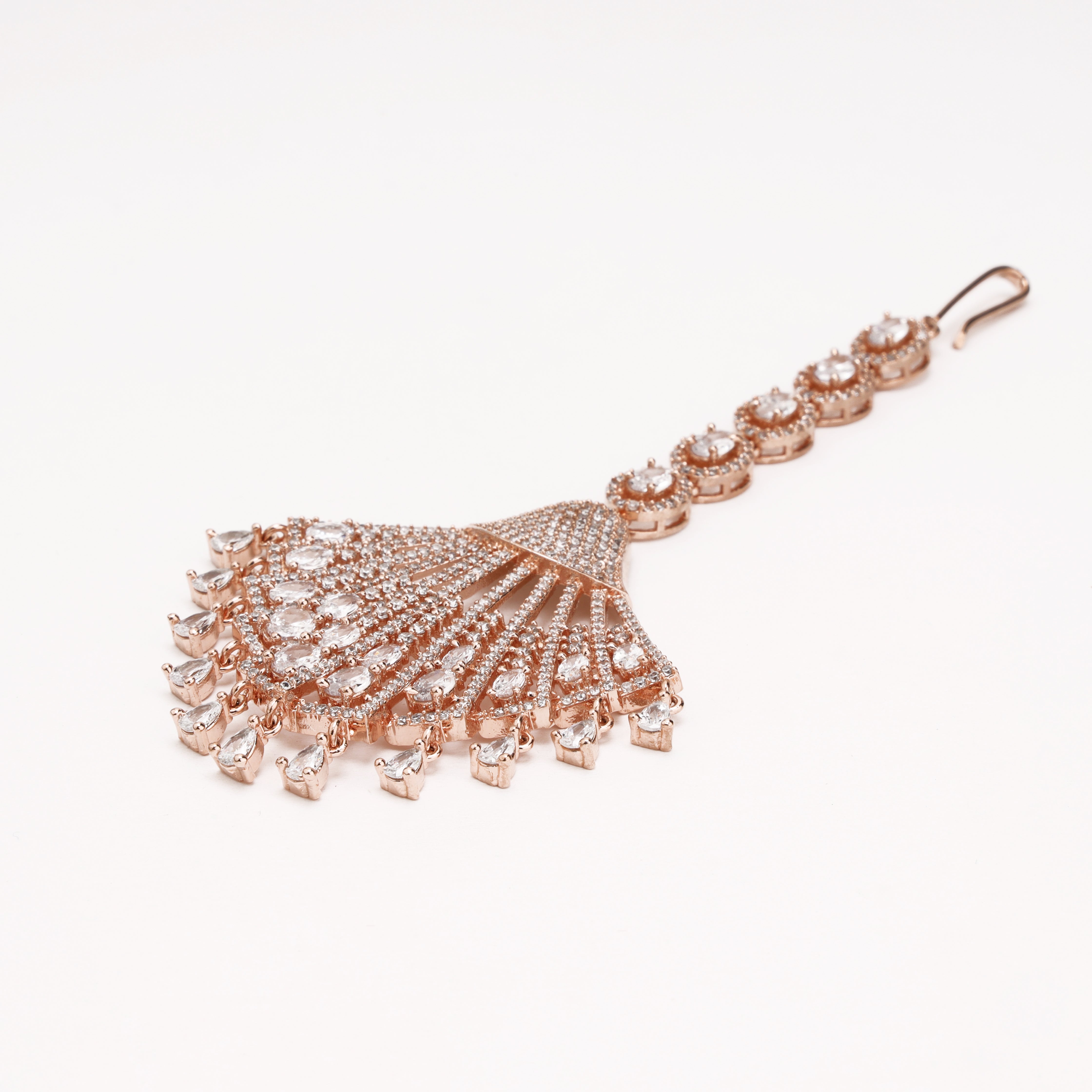 A rose gold maang tikka featuring a large, fan-shaped pavé crystal cluster with dangling crystal accents, connected to a straight bar with matching crystal-set rings and a hook clasp, shown on a plain white background.
