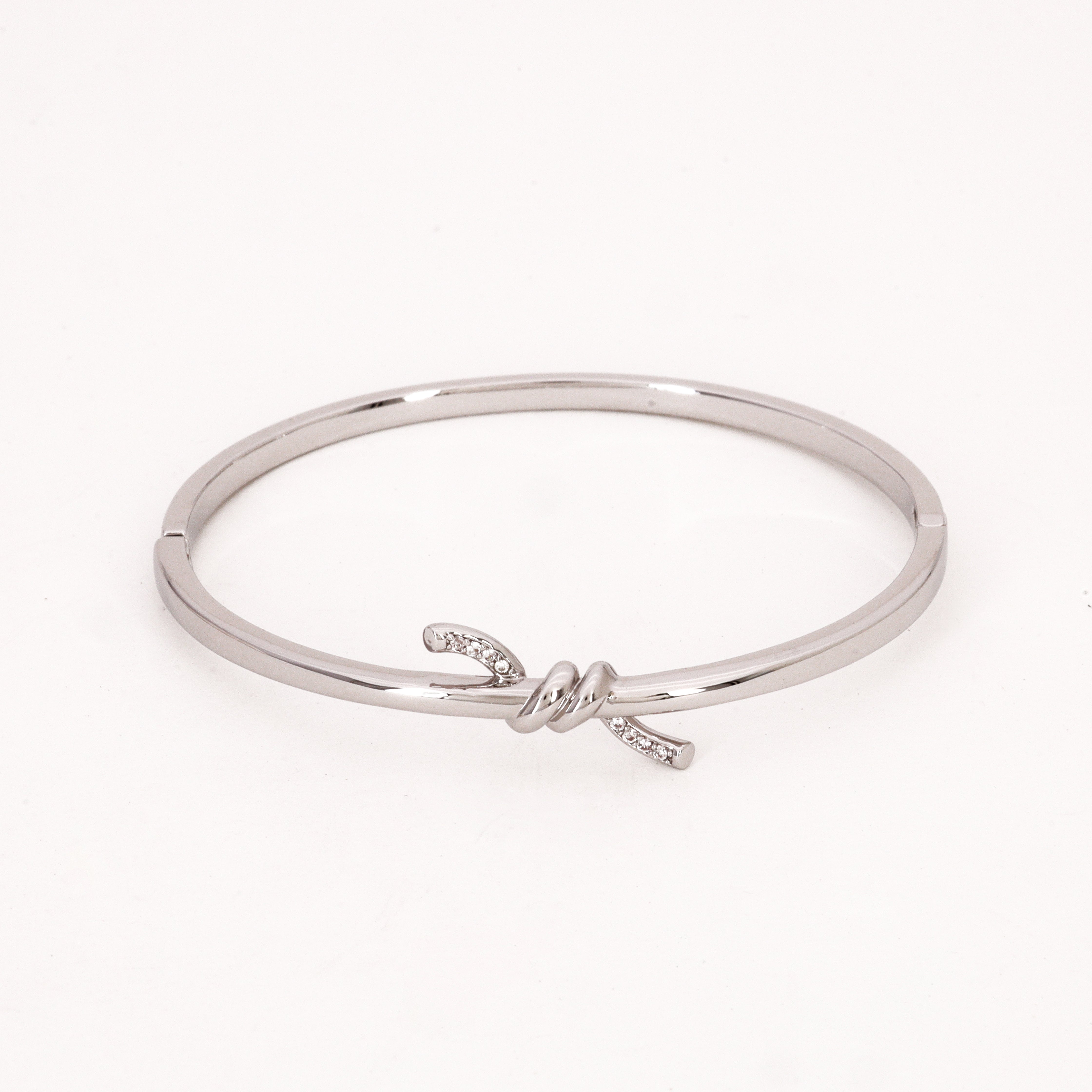 Silver Tone Crystal Knot Bracelet featuring a polished central knot with clear crystal encrusted ends on a white background for US Catalog.