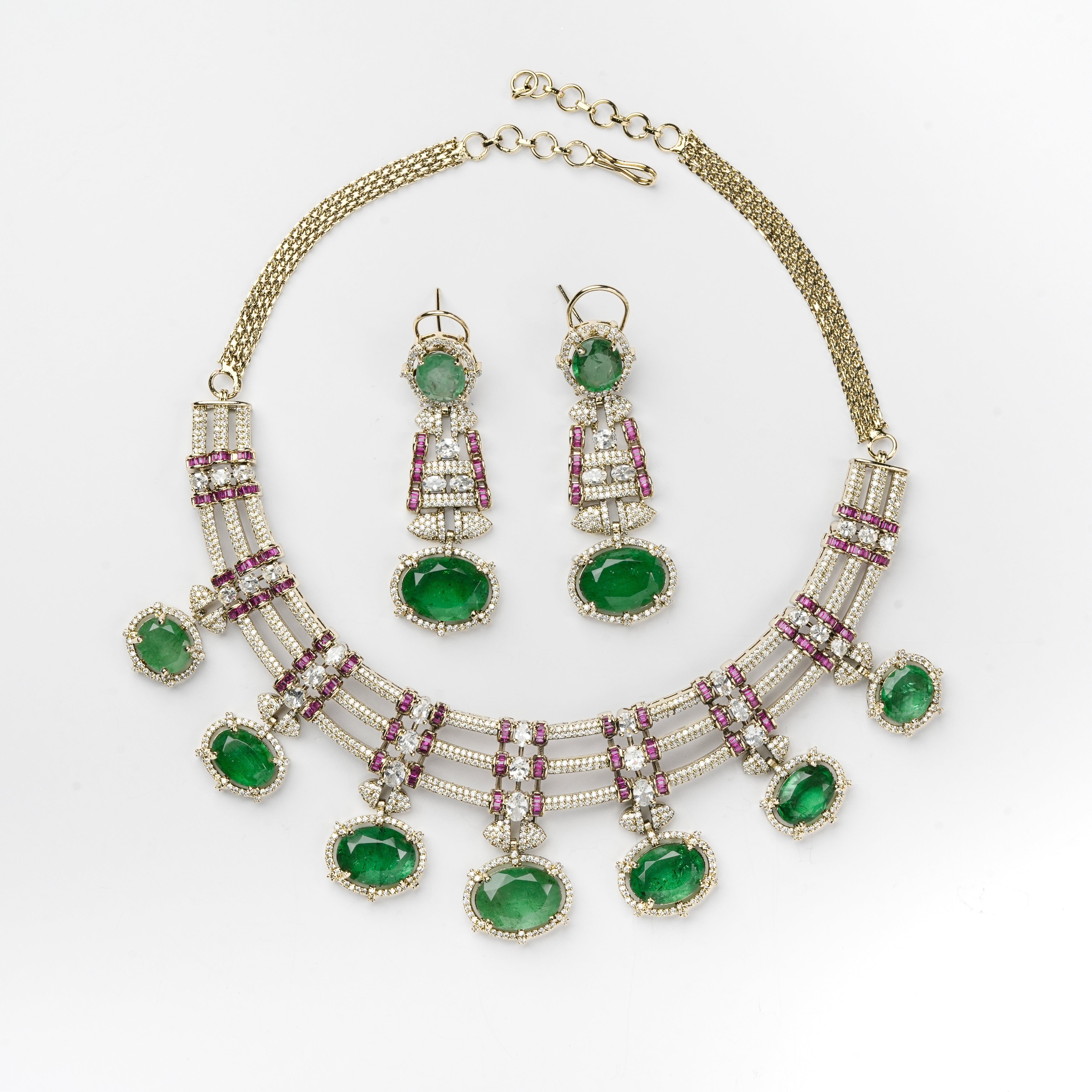 A gold-plated statement necklace and matching drop earrings set with oval green emerald-cut stones and rows of pink gemstones, displayed on a clean white background.