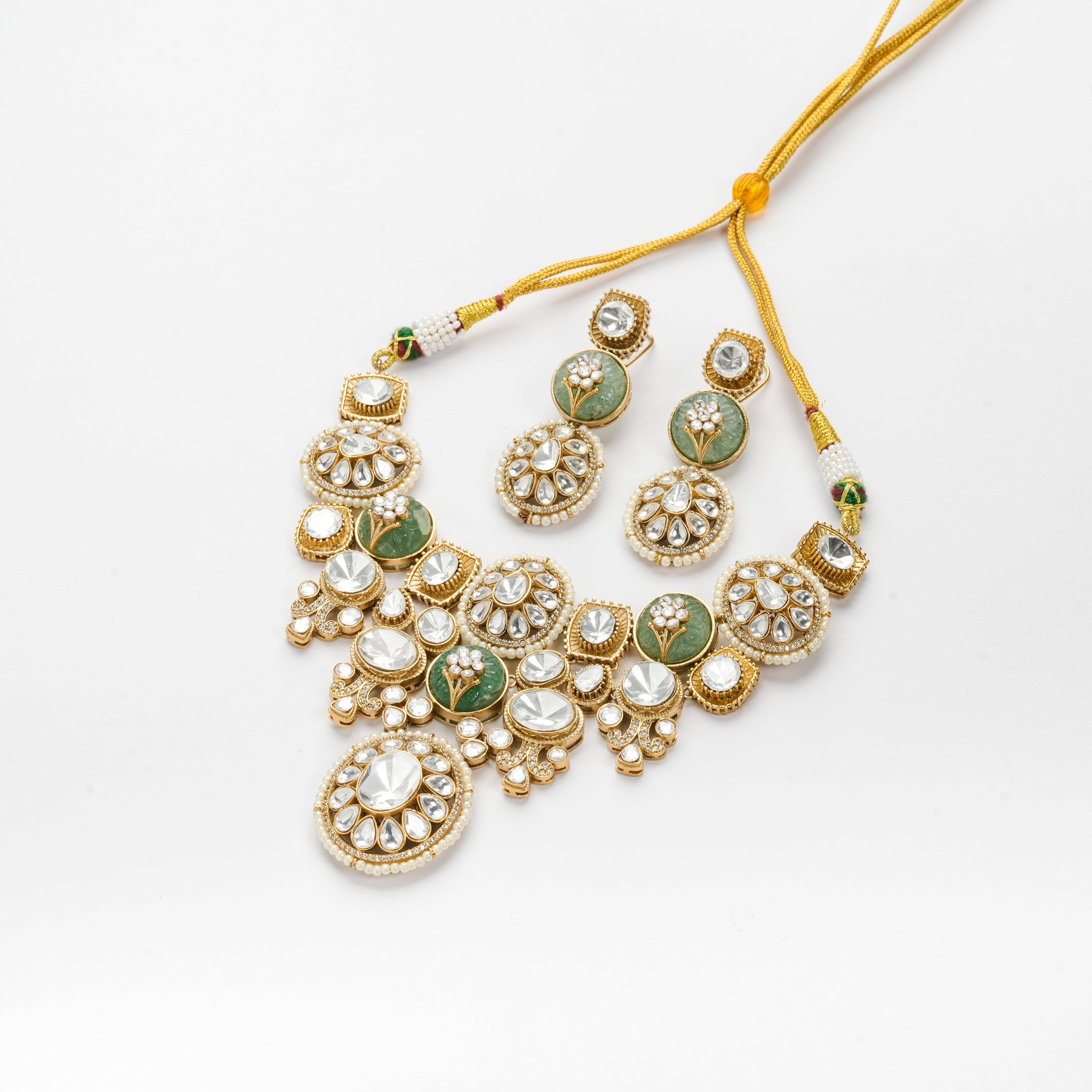 Gold-toned traditional Indian jewelry set featuring a statement necklace and matching earrings with green stone inlays and clear stones, displayed on a clean white background.