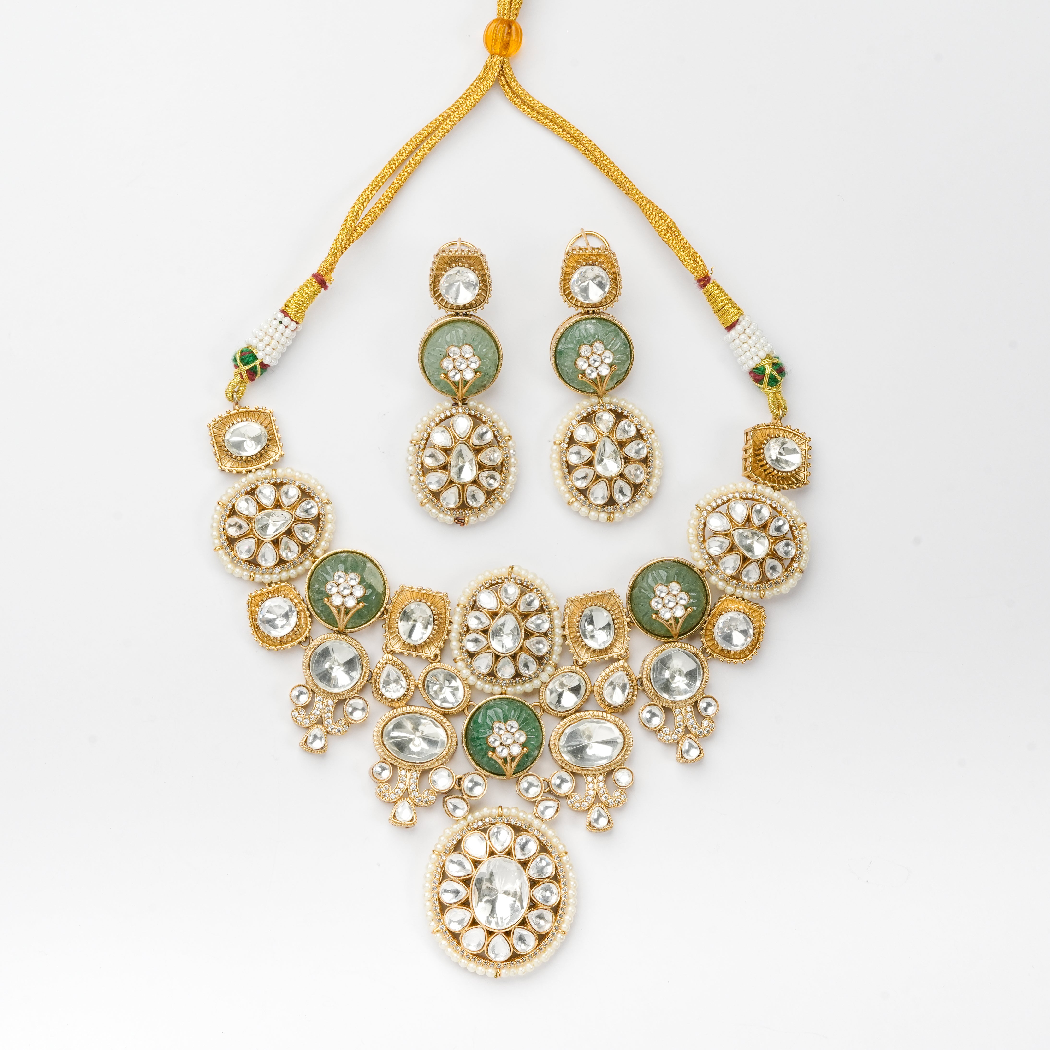 Gold-toned traditional jewelry set featuring a statement necklace and matching earrings, embellished with clear stones and green enamel details, displayed on a white background.