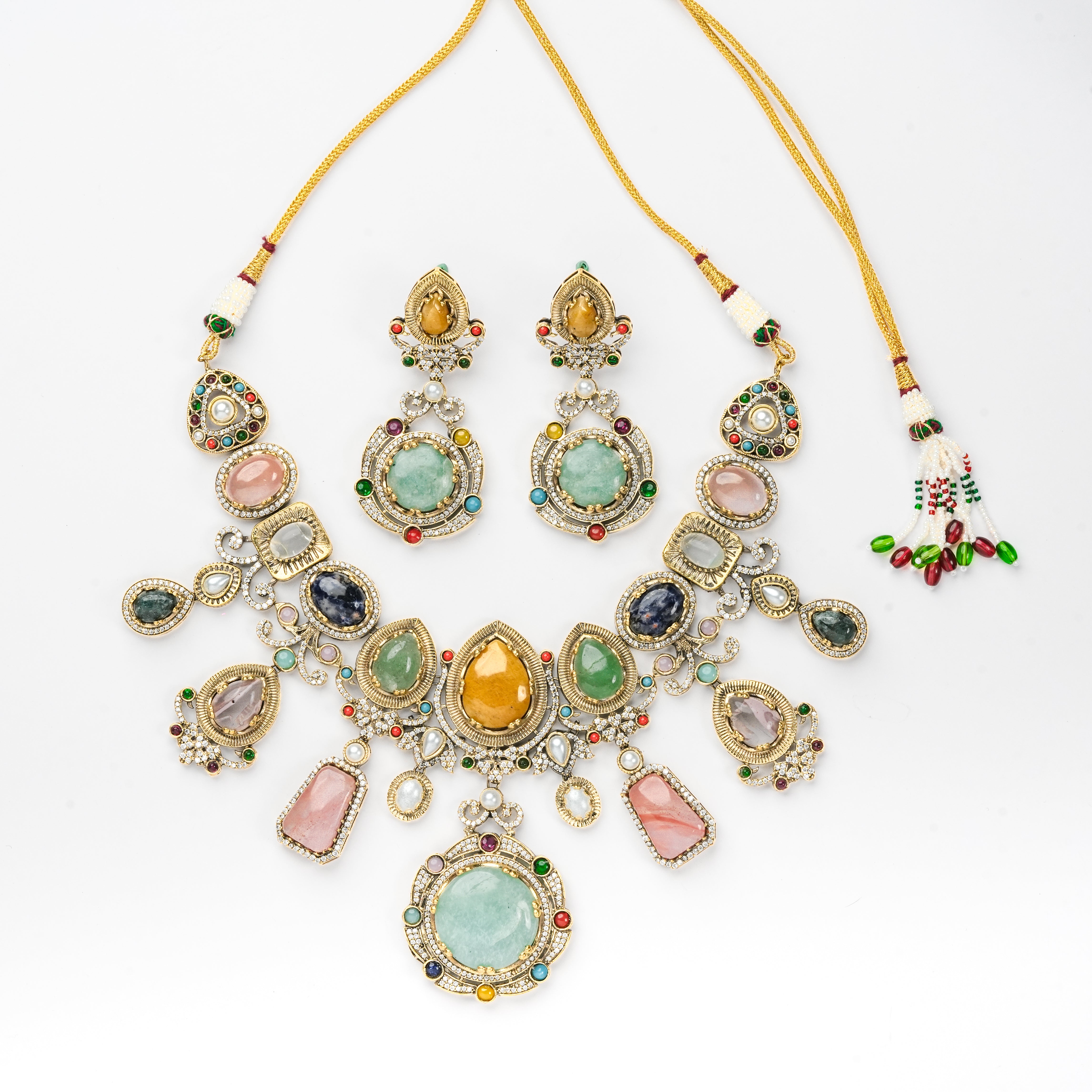 A gold-toned jewelry set featuring a statement necklace and matching drop earrings, embellished with multiple colorful gemstones including light green, pink, orange, blue, and red, displayed on a clean white background.