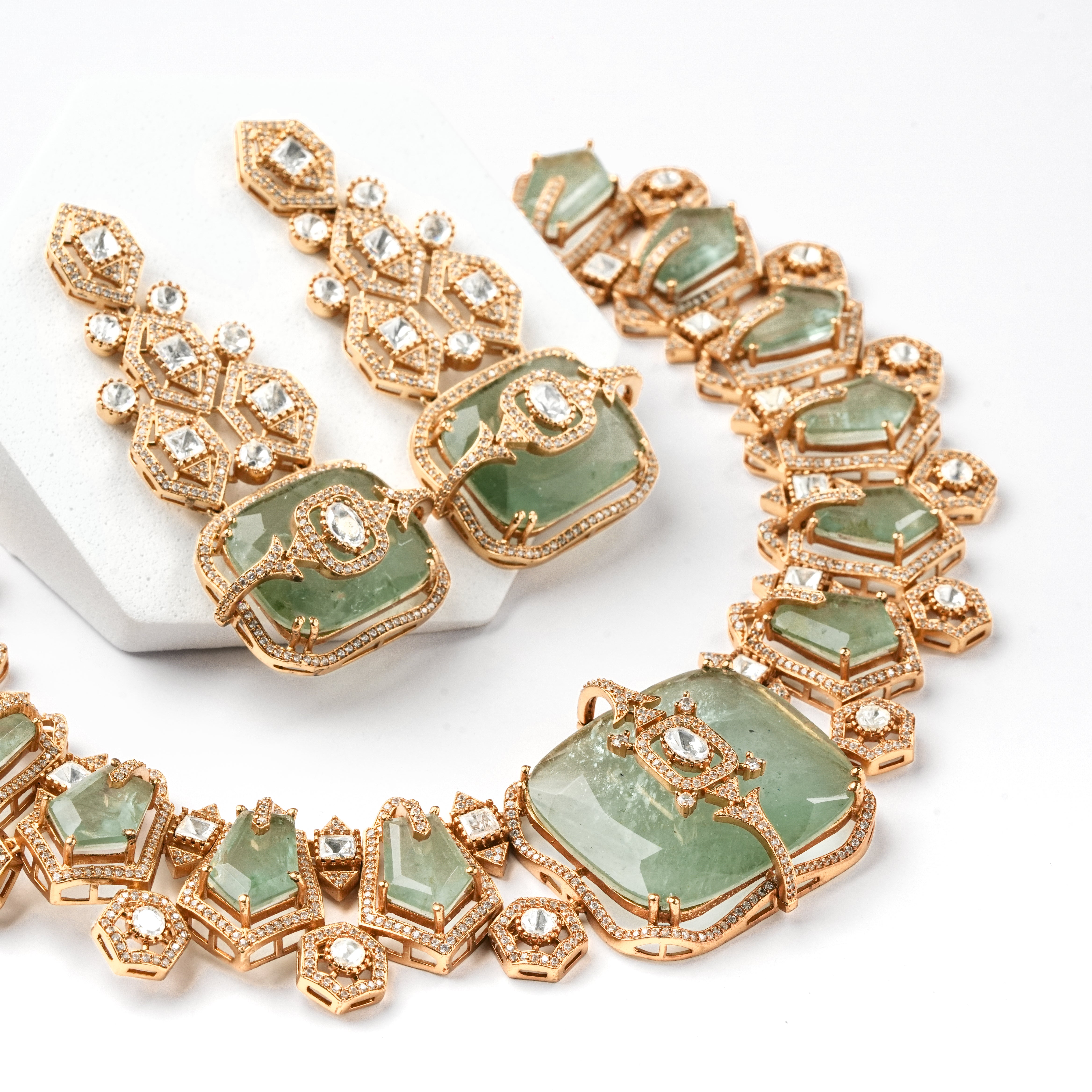 A gold-tone jewelry set featuring a statement necklace and matching drop earrings, embellished with light green stone inlays and clear rhinestones, displayed on a white background.