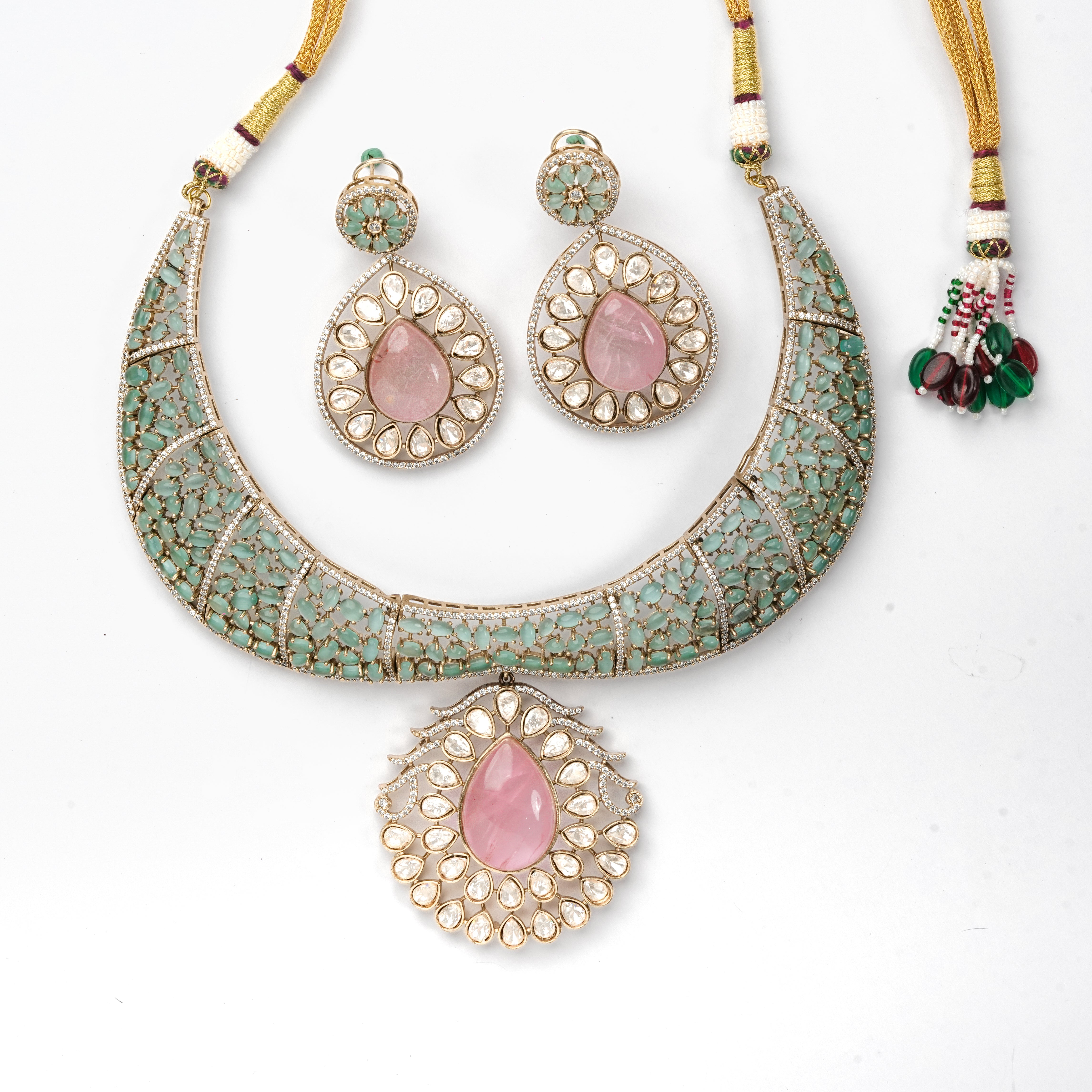 A traditional Indian jewelry set featuring a crescent-shaped necklace and matching earrings. The pieces are embellished with gold-plated metal, turquoise-colored stones, and central pink teardrop gemstones surrounded by small white stones.