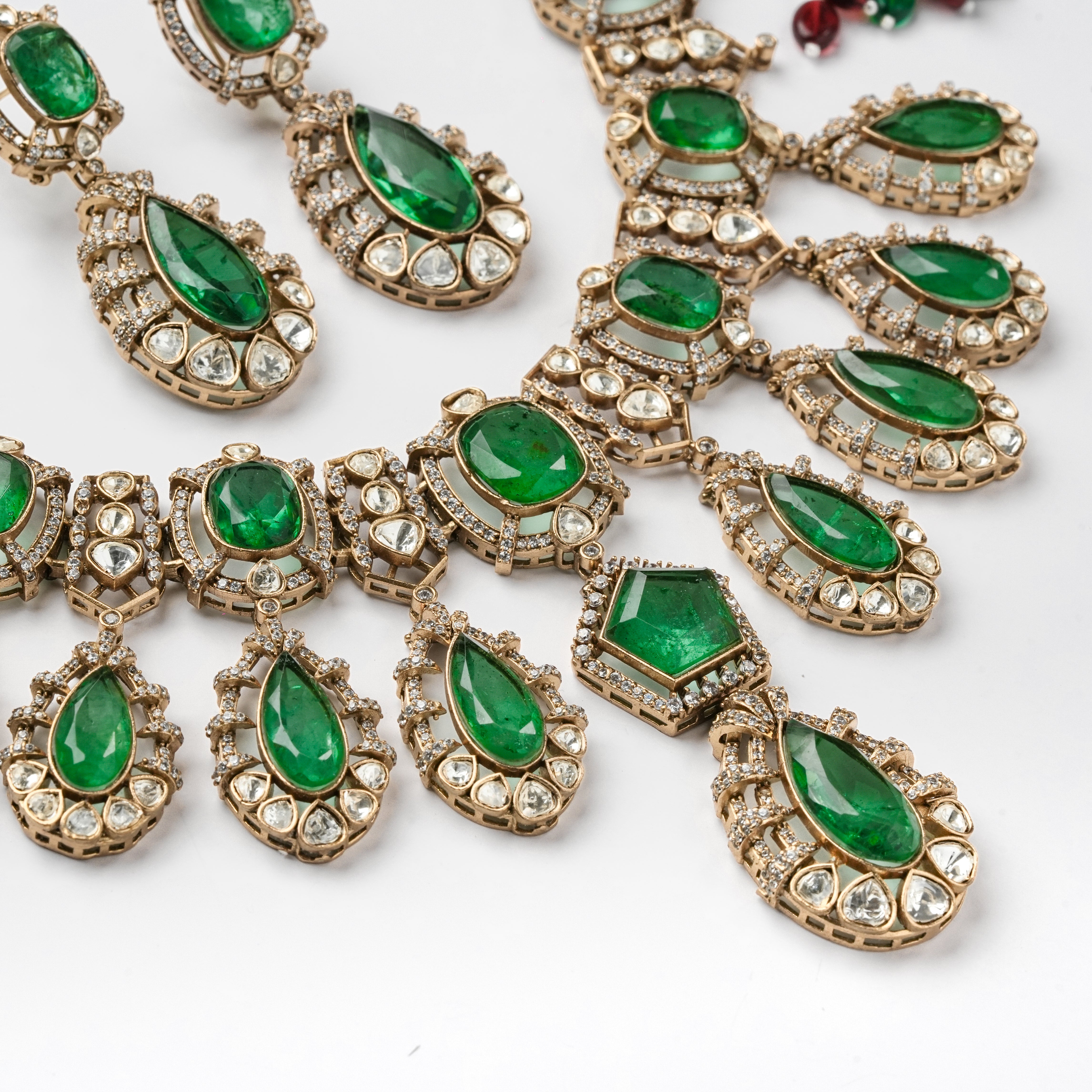 Antique gold finish green stone kundan polki necklace set with teardrop drops and matching drop earrings for bridal wear.