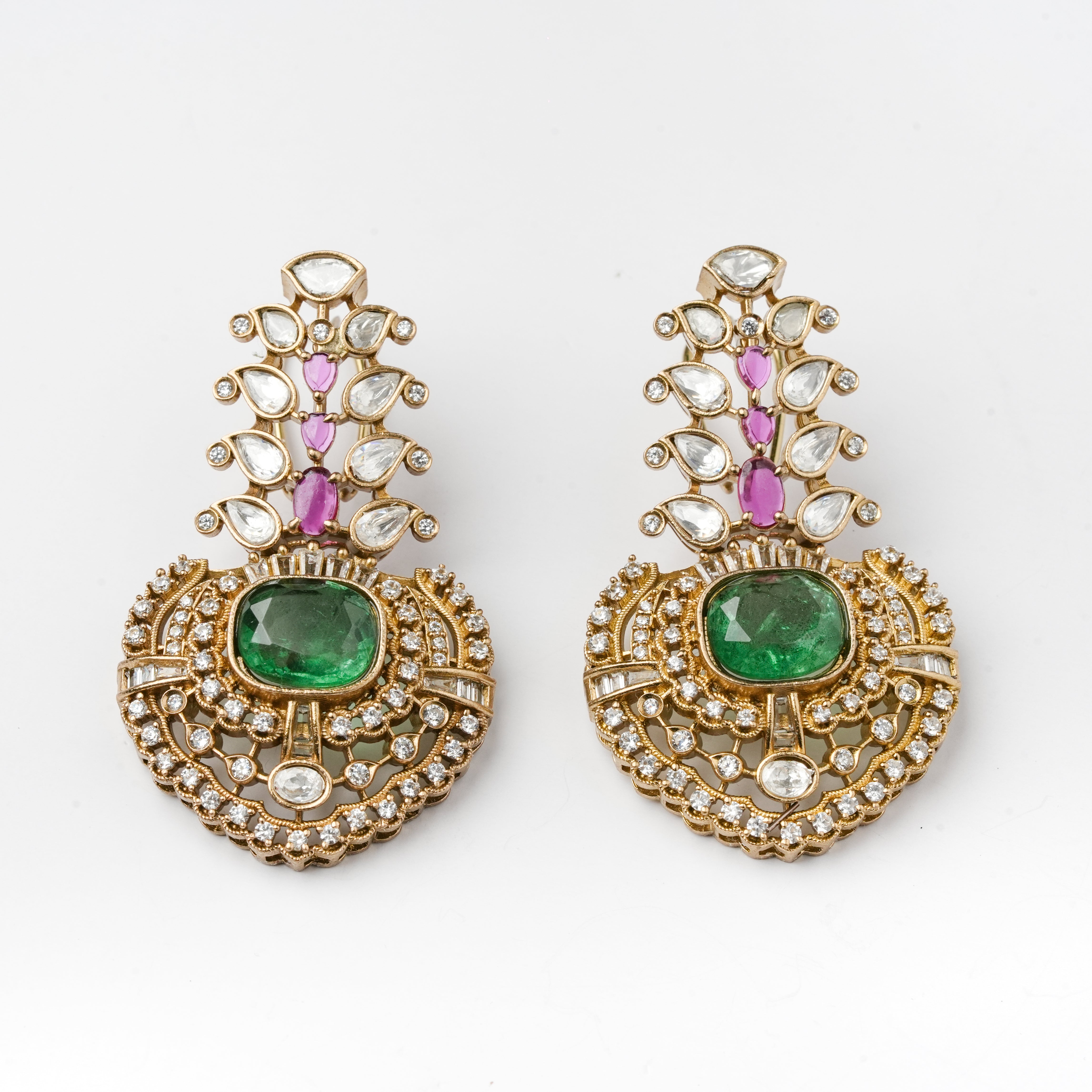 A pair of ornate gold-toned drop earrings with large green emerald-cut center stones, pink marquise-cut stones above, and clear round stones throughout, shown on a plain white background.