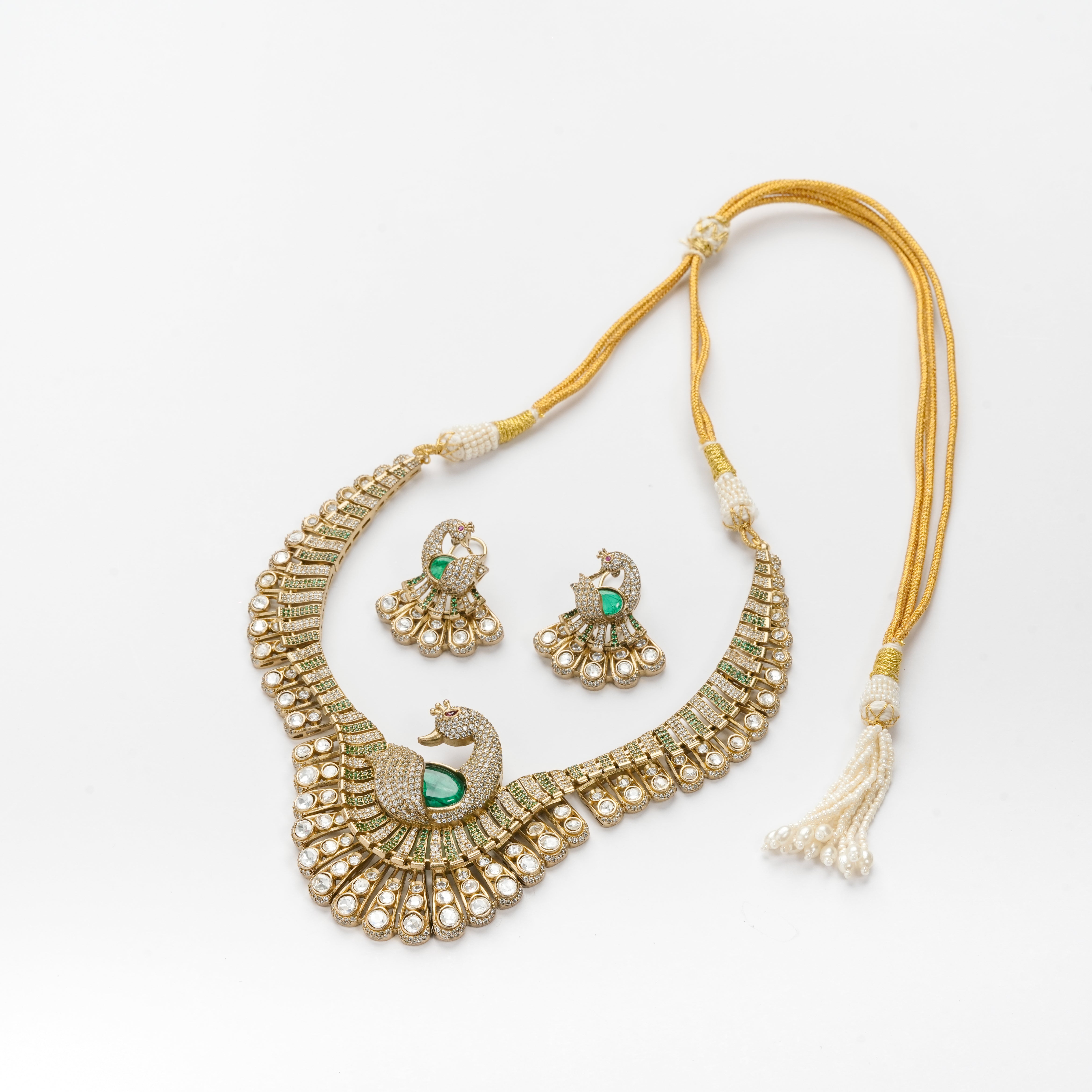 A gold and white beaded necklace set with matching earrings, featuring peacock motifs with green stone accents, displayed on a clean white background.