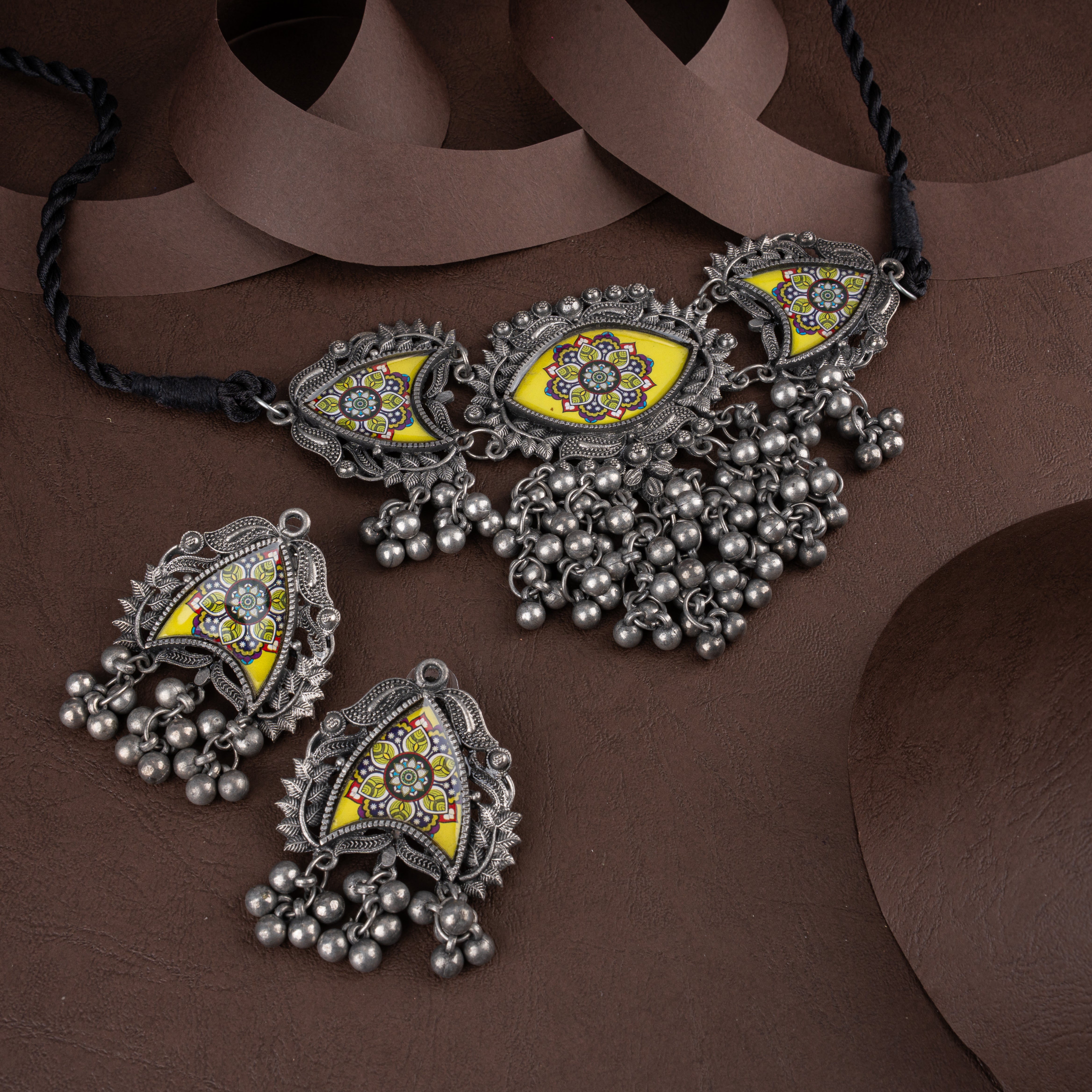Oxidised silver choker necklace and matching earrings featuring hand-painted yellow mandala floral prints and ghungroo beads on a brown background.