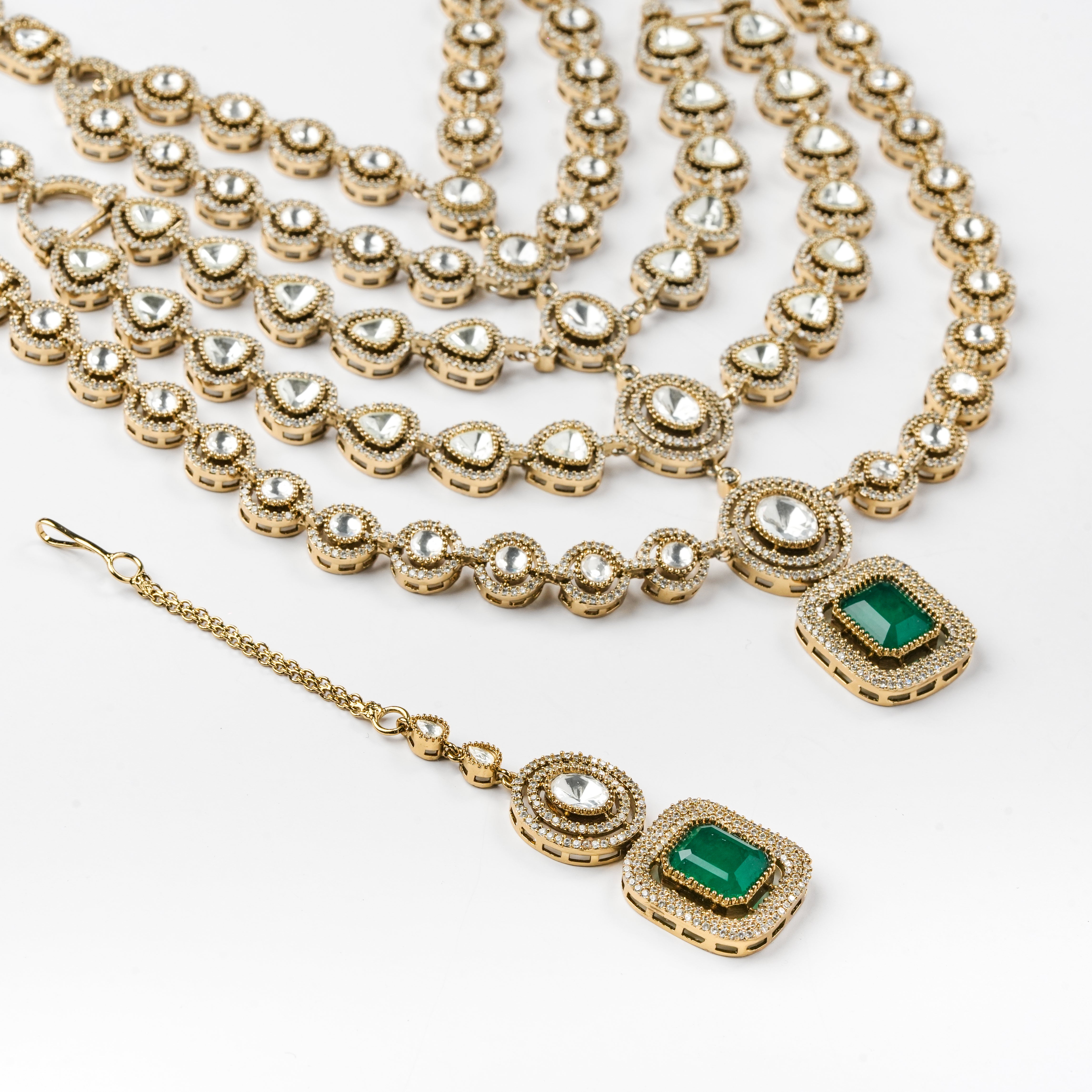 Gold-toned traditional jewelry set featuring a multi-strand necklace with heart-shaped motifs, a matching pendant with a green rectangular stone, and a matching dangling earring with a green square stone and clear stones, displayed on a white background.